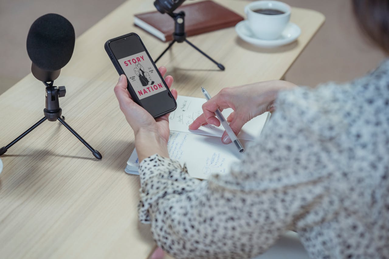 gallery-03 A woman records a podcast at a desk using a smartphone and microphones.