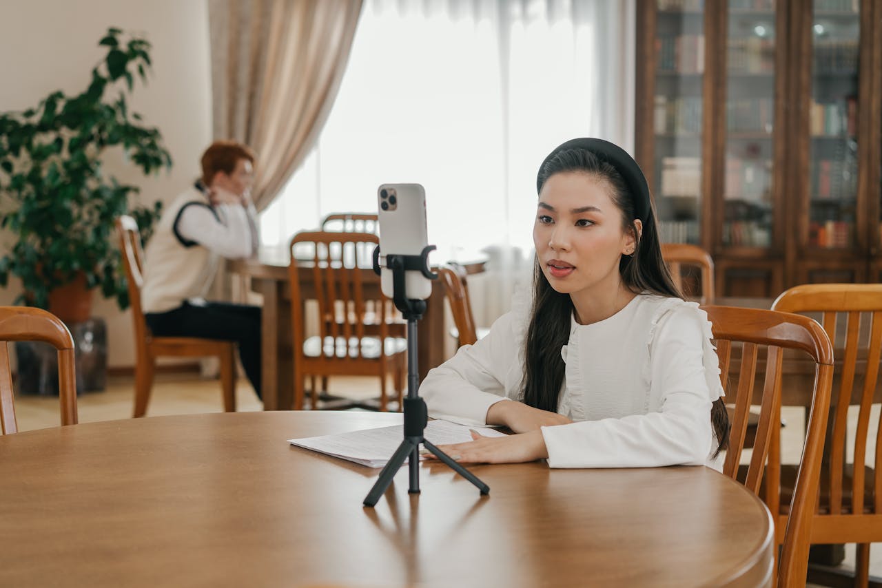 gallery-01 Young woman creating vlog content using a smartphone in a cozy indoor setting with wooden furniture.